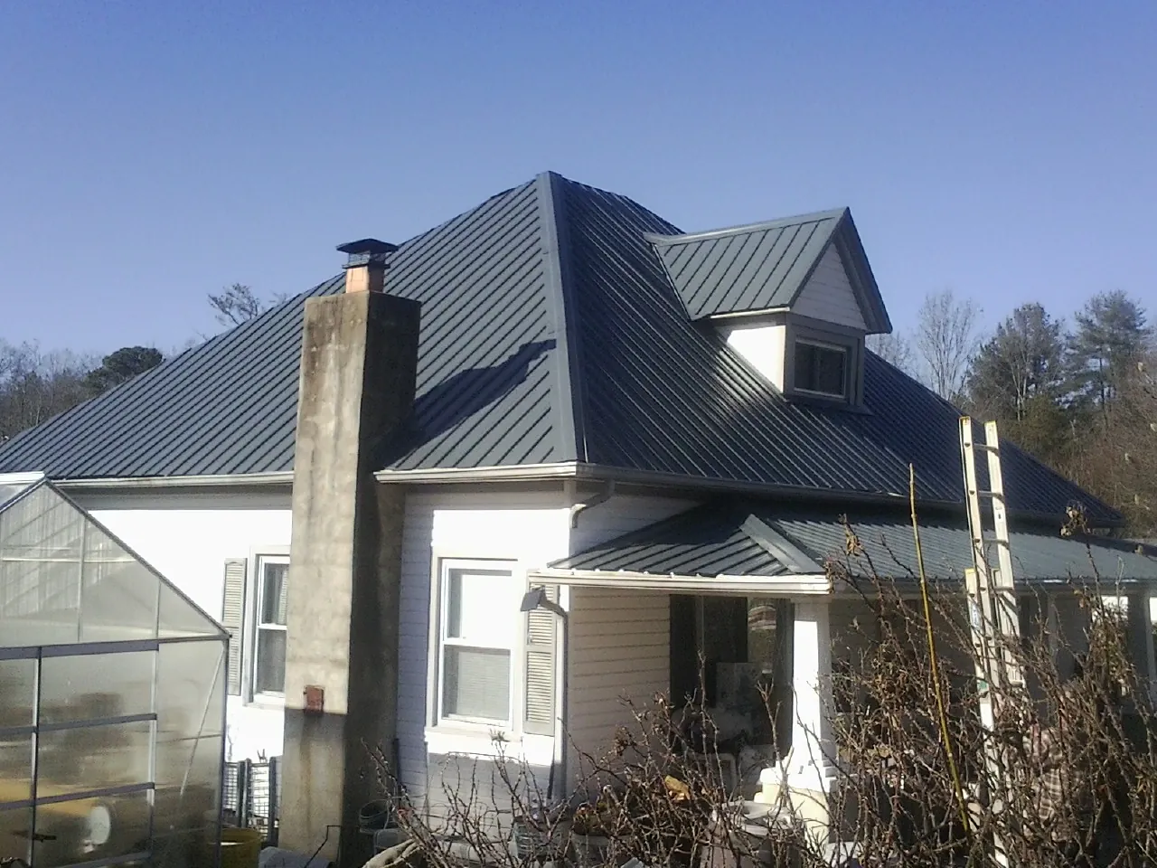 Dark blue standing seam metal roof on a white farmhouse with dormer — Slate & Tile Roof Repair by Roofing Brothers in Salado