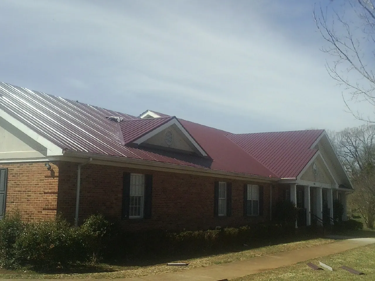 Red metal roof with gabled entries on a long brick building, from a Hail Damage Roof Repair job in Salado