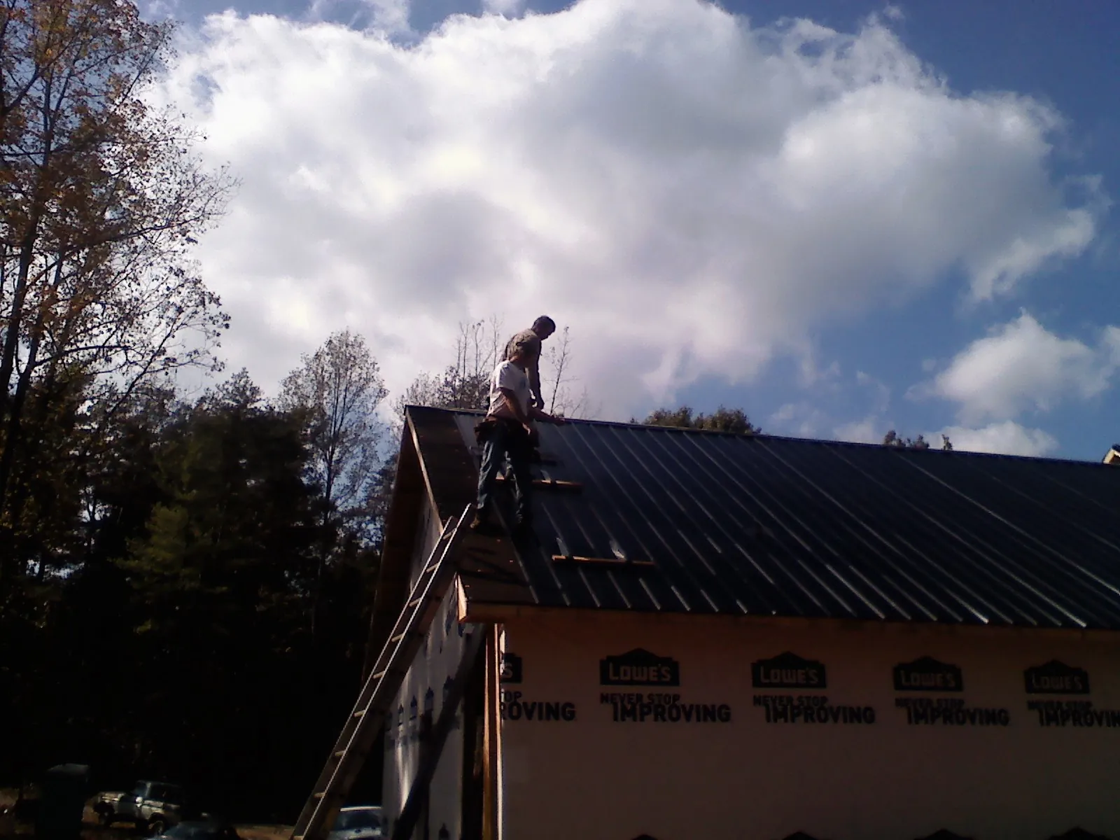 Roofer fastening dark metal panels high against a cloudy sky, from a Roof Inspection job in Salado